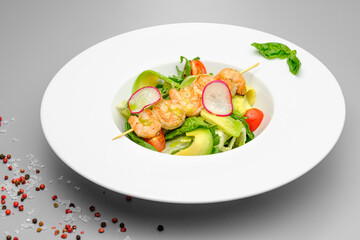 Grilled shrimp on a skewer with vegetables on a white plate on a gray background.
