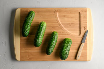 Four fresh green cucumbers on a cutting board and a knife on a light gray background. Top view