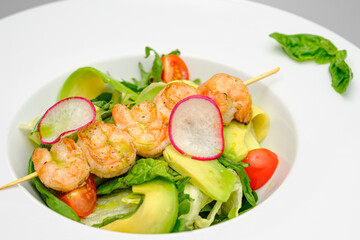 Grilled shrimp on a skewer with vegetables on a white plate on a gray background.
