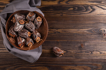 Dried persimmon in brown bowl on wooden background. Top view, copy space.