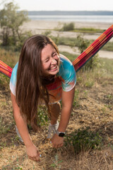 laughing girl lay down on a hammock across, dangling her arms down, cheerful outdoor recreation