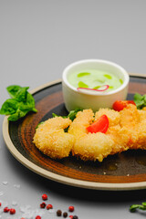 Shrimp fries in breadcrumbs on a gray background decorated with basil, sea salt and pepper. Snacks on the restaurant menu.
