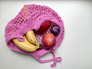 Cotton mesh bag with fruit on a white background. Bananas, apples, plums in a pink string bag. Zero waste, no plastic concept. A summer refreshing food
