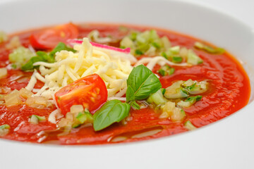 Tomato soup minestrone with cheese in a white plate on a gray background.