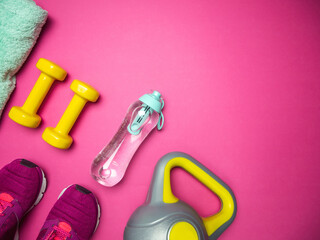 Dumbbells, kettlebell, training shoes, filtered water bottle and towel. Fitness flat lay composition with copyspace on pink background.