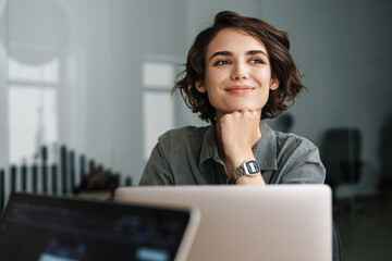 Image of young beautiful joyful woman smiling while working with laptop - 368228583