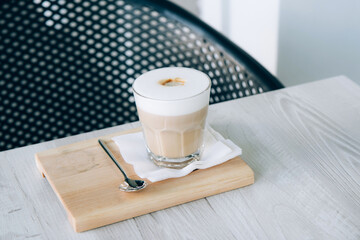 Latte or Cappuccino in a glass cup on a wooden tray. Morning coffee with foam on a wooden table