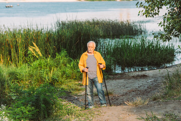 Senior man holding walking sticks on path in summer park
