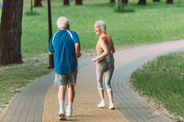 Back view of smiling senior woman looking at husband while jogging in park