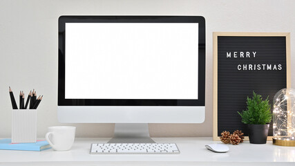 Office creative desk with blank screen computer, letter board, lightbulb, pine cone, tree and coffee cup on white table in home office. Christmas Day concept.