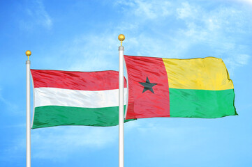 Hungary and Guinea-Bissau two flags on flagpoles and blue cloudy sky