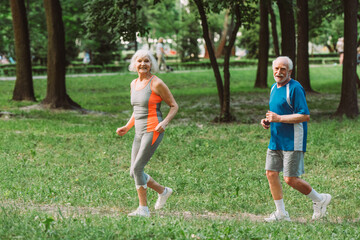 Positive senior coupe looking at camera while jogging in park