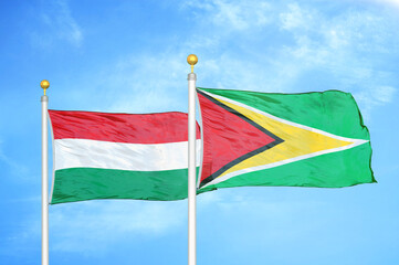 Hungary and Guyana two flags on flagpoles and blue cloudy sky