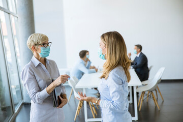 Two businesswomen talking in the office and wearing mask as a virus protection