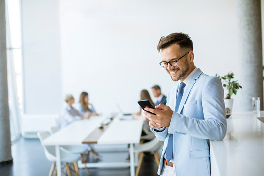 Happy young man using his mobile phone and smiling while his colleagues working in the background