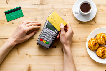 Payment transactions. Hand hold card near terminal on wooden cafe table top-down