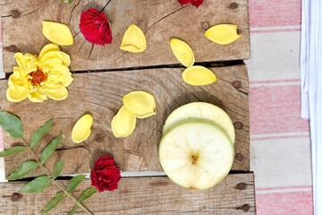 apple slices, yellow and red roses petals on wooden background, top view. 