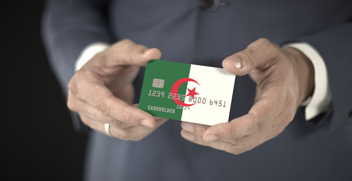 Businessman takes plastic bank card with printed flag of Algeria, fictional numbers