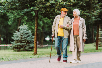 Senior couple smiling while walking on path in park - Powered by Adobe