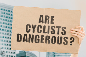 The question " Are cyclists dangerous? " on a banner in men's hand with blurred background. Cycling. Environmentally sustainable transport. Transportation. Safety. Danger. Violation the rules. Road 