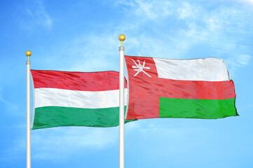 Hungary and Oman two flags on flagpoles and blue cloudy sky