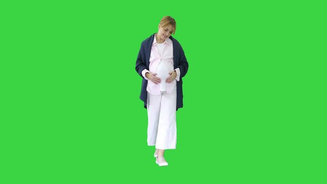 Happy and proud pregnant woman looking at her belly while walking on a Green Screen, Chroma Key.