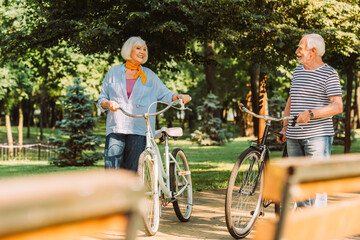 Obraz premium Selective focus of positive senior couple with bicycles walking in park