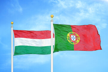 Hungary and Portugal two flags on flagpoles and blue cloudy sky
