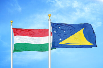 Hungary and Tokelau two flags on flagpoles and blue cloudy sky