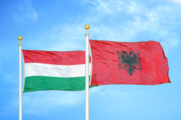Hungary and Albania  two flags on flagpoles and blue cloudy sky