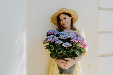 Portrait of a woman in a yellow dress and stray summer hat holding a large bouquet of purple flowers, smiling 