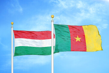 Hungary and Cameroon  two flags on flagpoles and blue cloudy sky