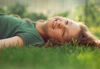 Happy smiling relaxing casual kid girl lying on the grass on nature summer background. Closeup positive outdoors