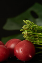 Washed tomatoes and asparagus in drops of water lie on a dark background Vertical Close up
