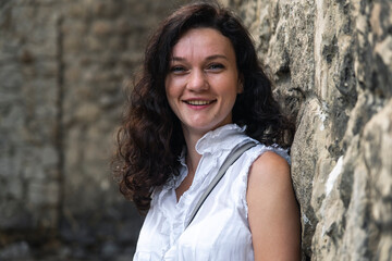 Portrait close up of young beautiful brunette woman with curly hair, on summer street background.