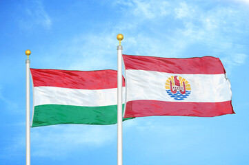 Hungary and French Polynesia two flags on flagpoles and blue cloudy sky