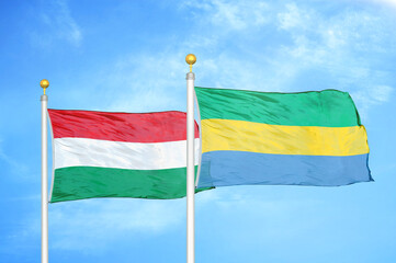 Hungary and Gabon two flags on flagpoles and blue cloudy sky