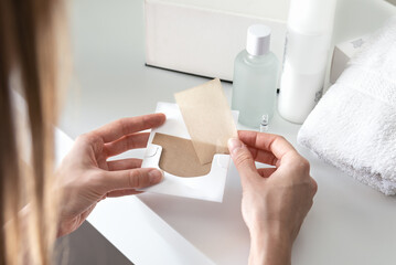 Female hands holding blotting paper with cosmetics at background