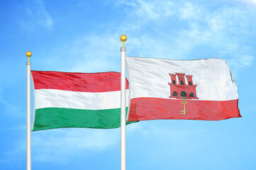 Hungary and Gibraltar two flags on flagpoles and blue cloudy sky