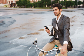 Pleased smiling business man using smartphone on a bicycle