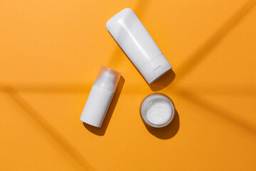 White blank cosmetic products bottles on orange background with free space for text, as advertisement.