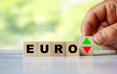 The hand turns the wooden cube with text EURO and red / green arrow as growth or crisis euro currency.