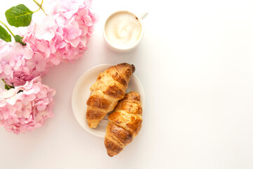 Feminine background of breakfast. Croissant and a cup of coffee with pink hydrangea. Copy space.