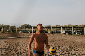 A young handsome caucasian man in swimming underpants on the beach with a volleyball in his hand. Sea and fun