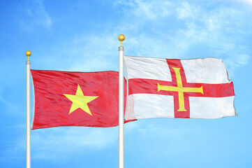 Vietnam and Guernsey two flags on flagpoles and blue sky