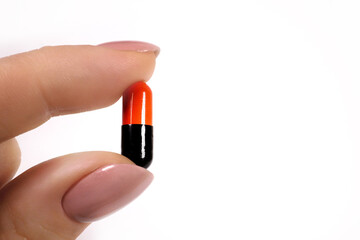 hand of a woman holding a pill, isolated against white background. close-up. black and red pilis. banner. space for text on the right