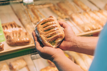 A man holds fresh baked goods in his hands in a supermarket.