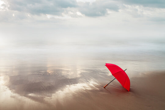 paraguas rojo en la orilla del mar con un cielo cargado en un amanecer