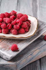 Raspberry fruits in plate on old cutting boards, healthy pile of summer berries on grey wooden background, angle view macro