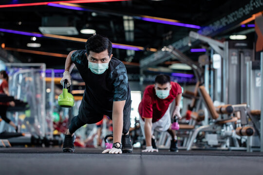 young mam and friend working out wearing surgical mask & latex rubber gloves, COVID-19 pandemic social distancing rules while working out in  a gym, new normal & social distancing concept